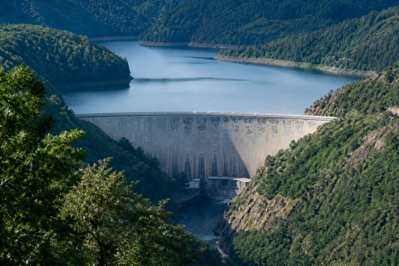 Grand barrage en béton retenant une rivière dans des gorges boisées