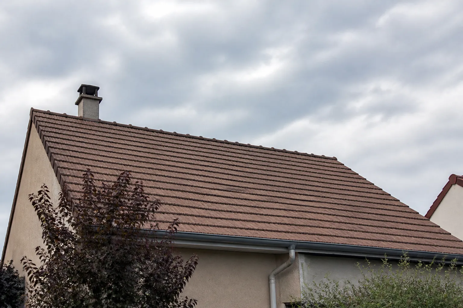 Toiture pentue et gouttières vues depuis la rue après un coup de vent