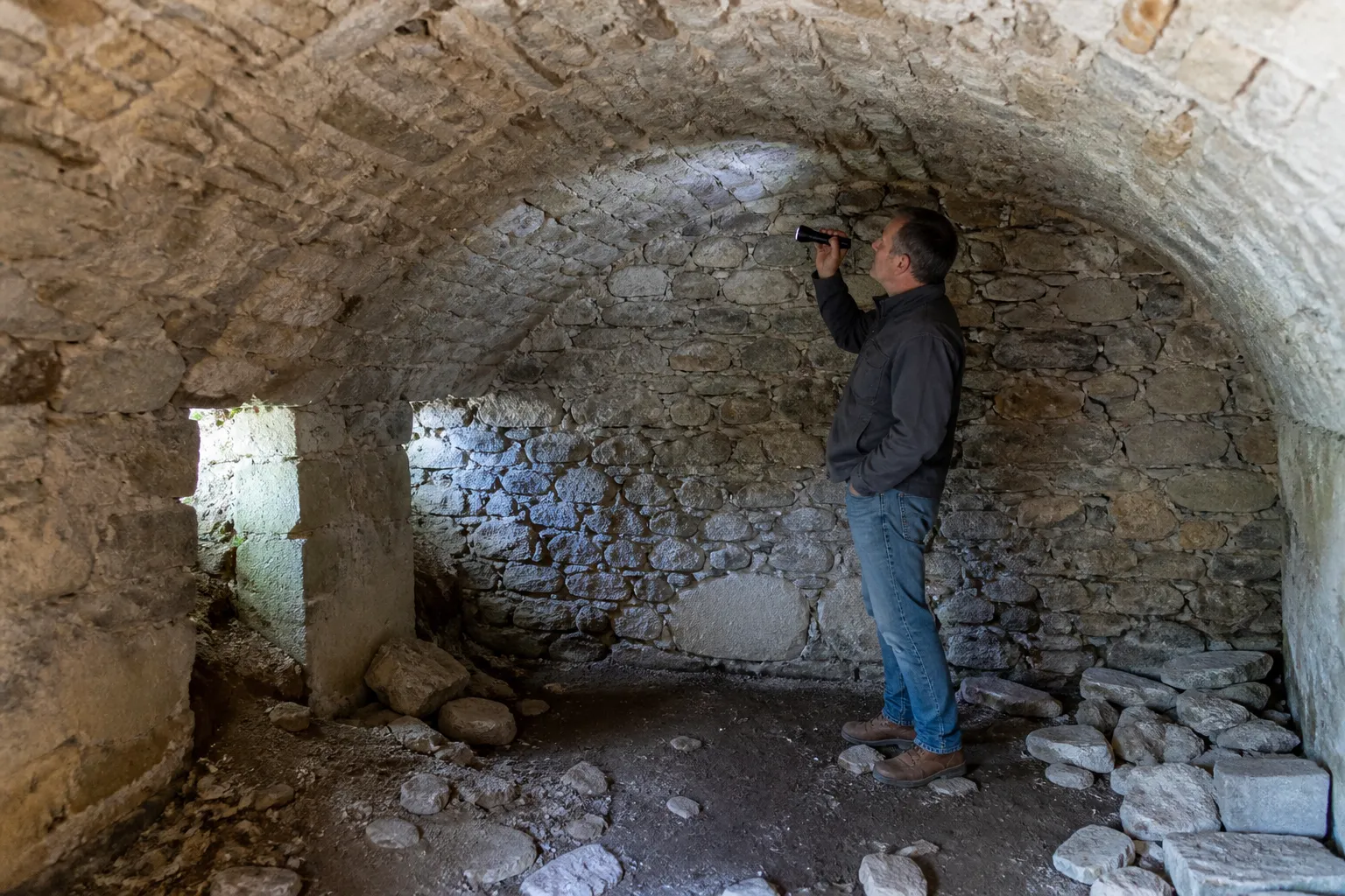 Expert en bâtiment examinant une cave voûtée en pierre avec une lampe