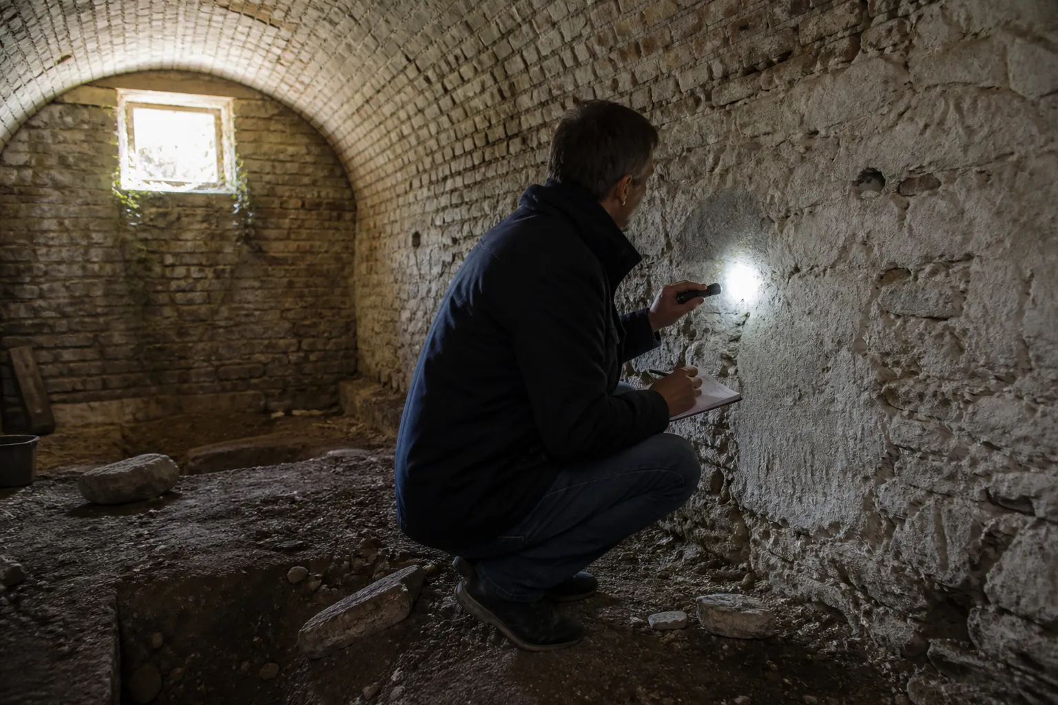 Expert observant une fissure sur un mur de cave voûtée à la lampe