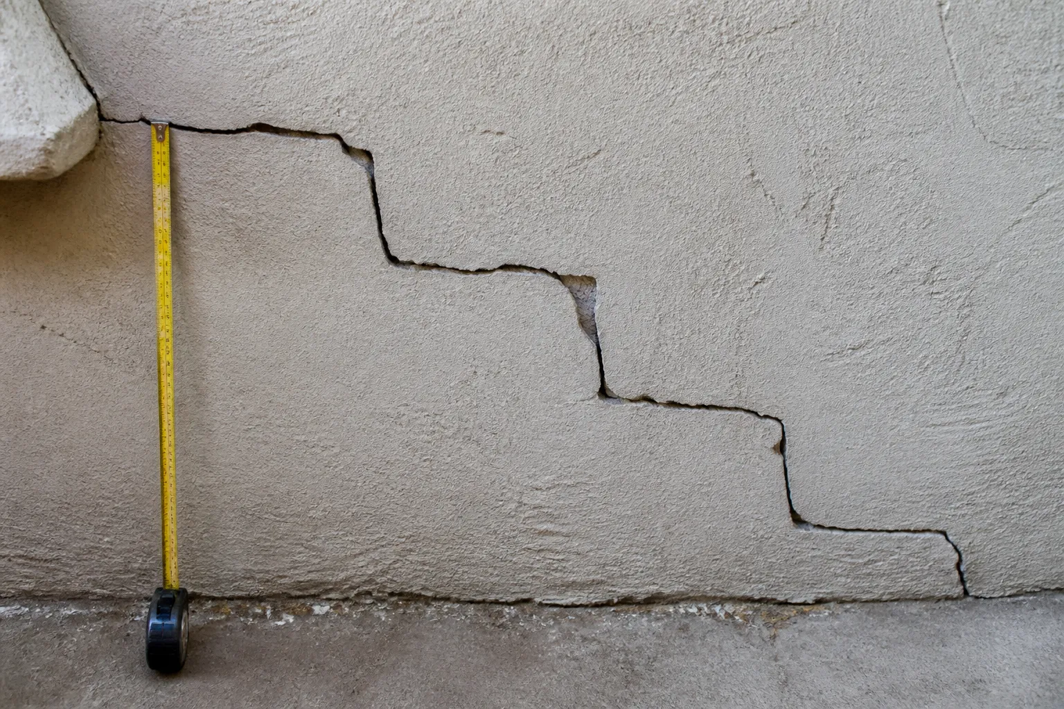 Fissure en escalier sur un mur en parpaings photographiée de près avec un mètre