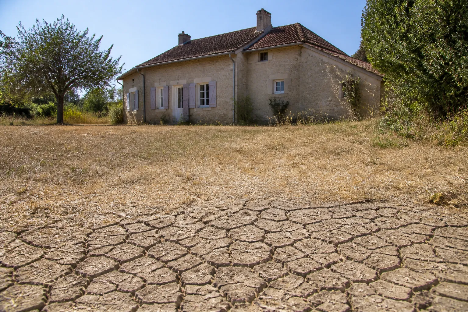 Maison individuelle du Berry avec sol argileux craquelé par la sécheresse au premier plan