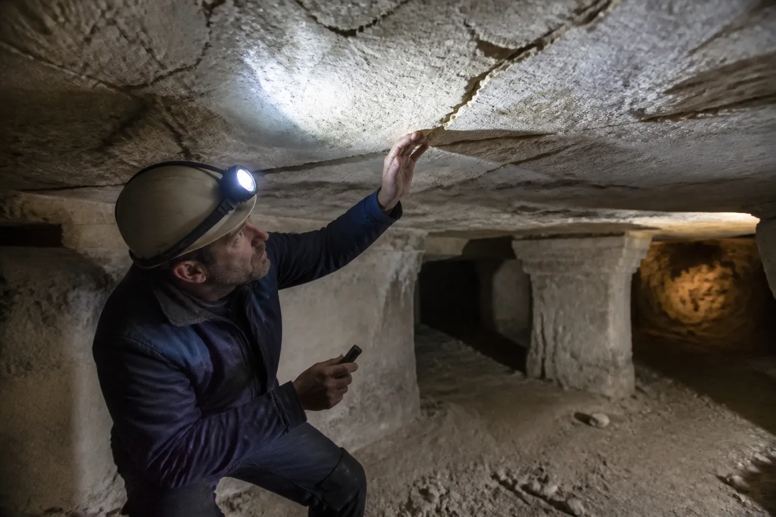 Expert en bâtiment examinant une fissure au plafond d’une cave creusée dans le tuffeau