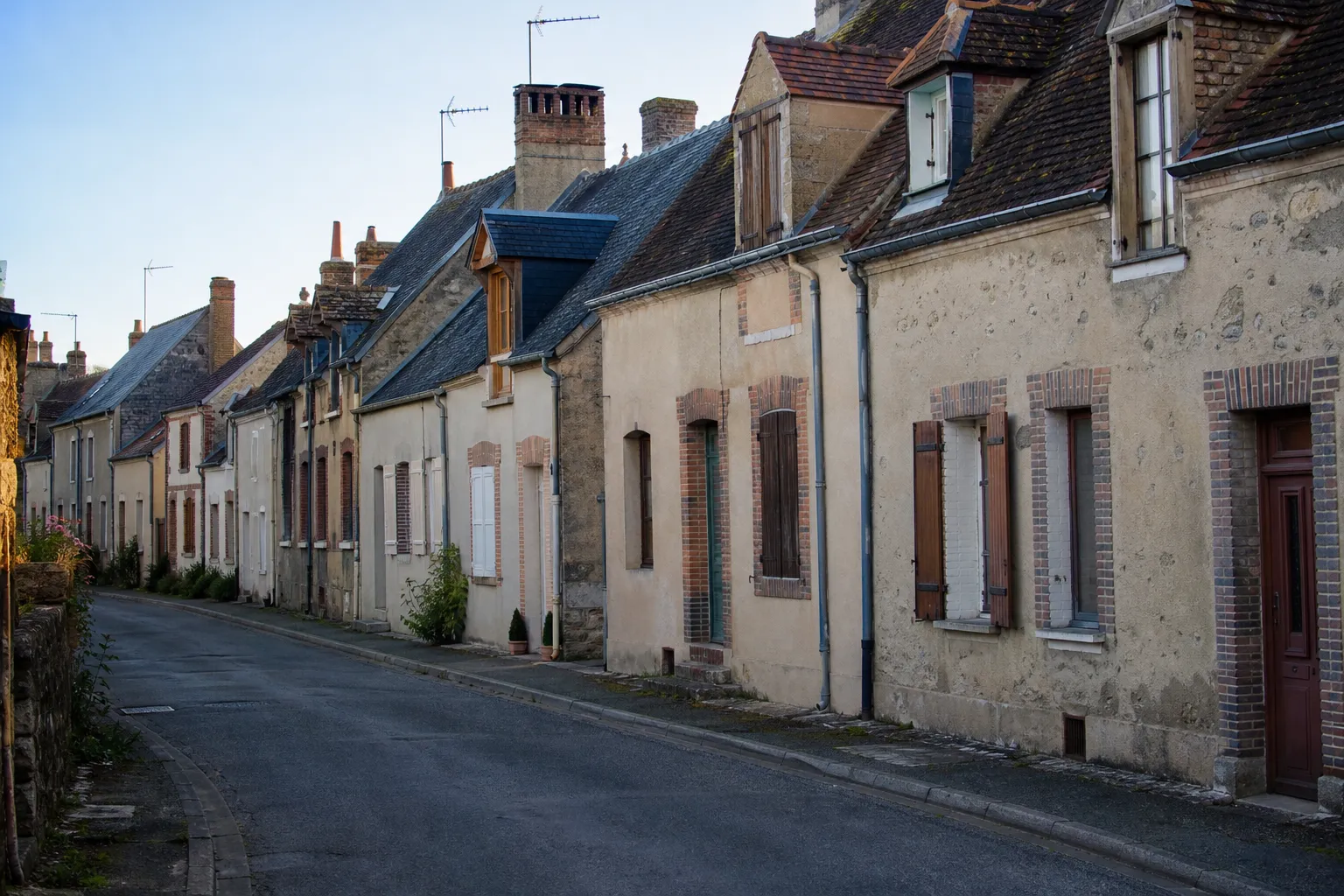 Rue de bourg avec maisons anciennes mitoyennes en pierre enduite et toits d’ardoise