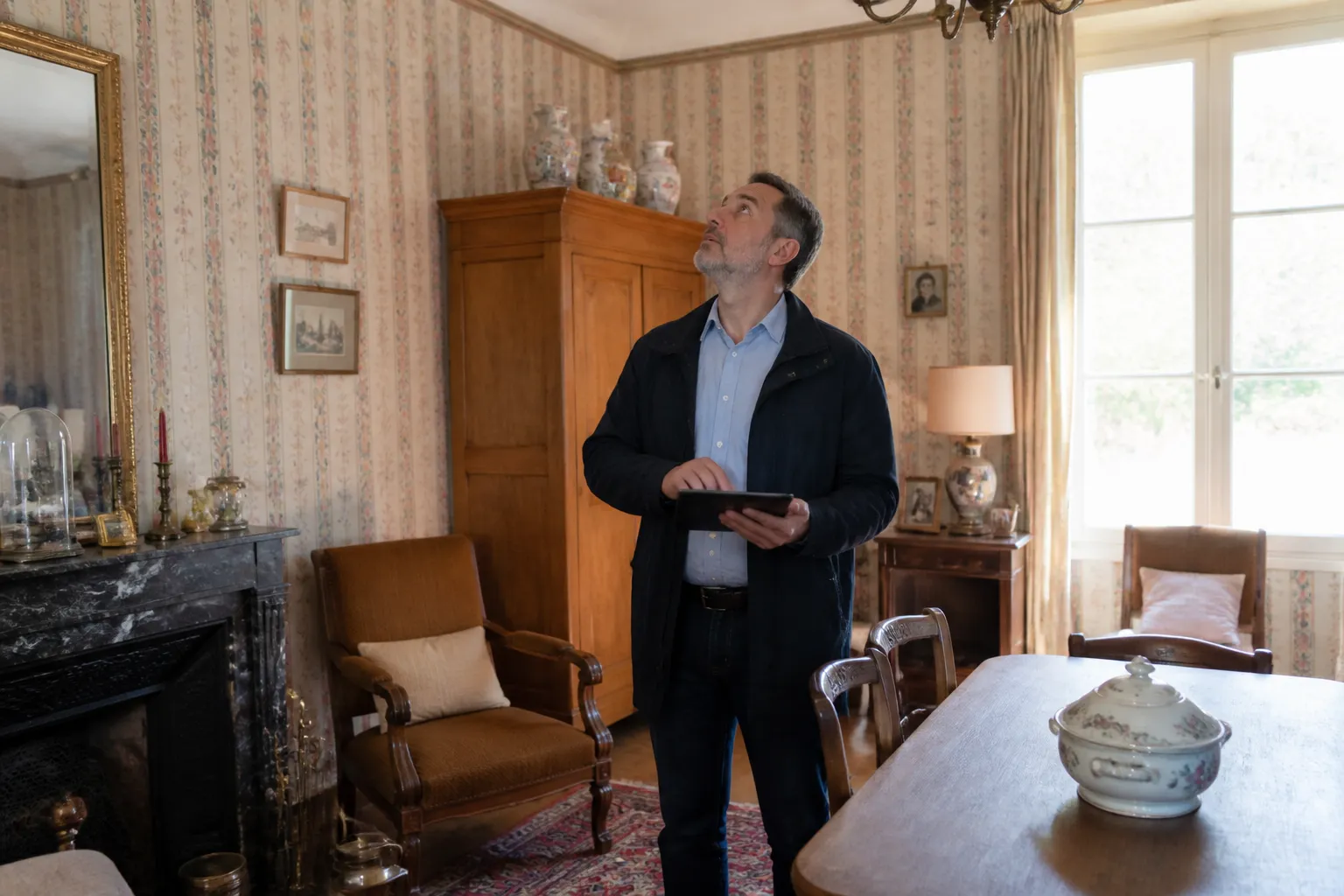 Expert en bâtiment inspectant le séjour d’une maison familiale ancienne encore meublée, vendue par des héritiers