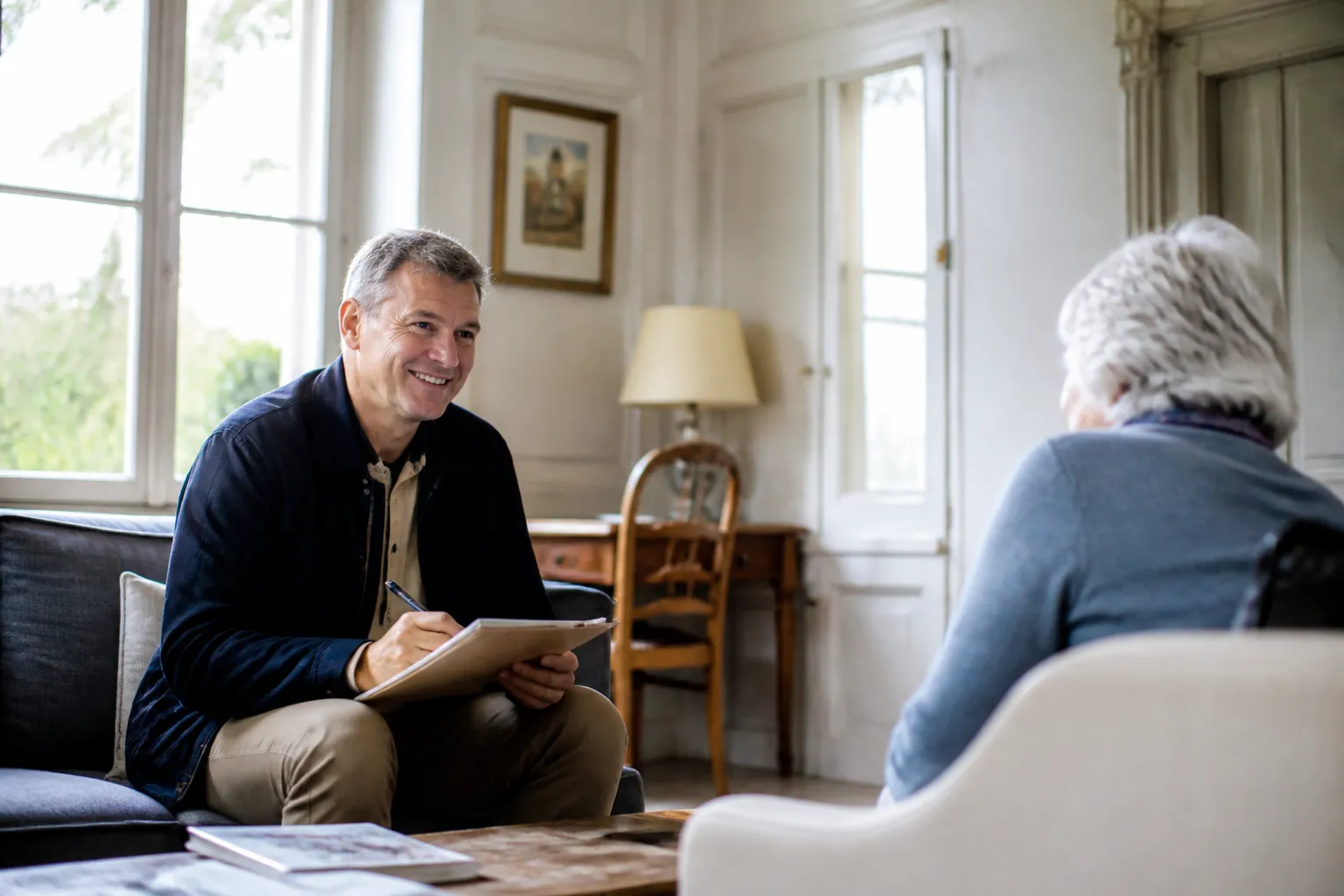 Expert en bâtiment échangeant avec une propriétaire âgée dans le salon de sa maison vendue en viager
