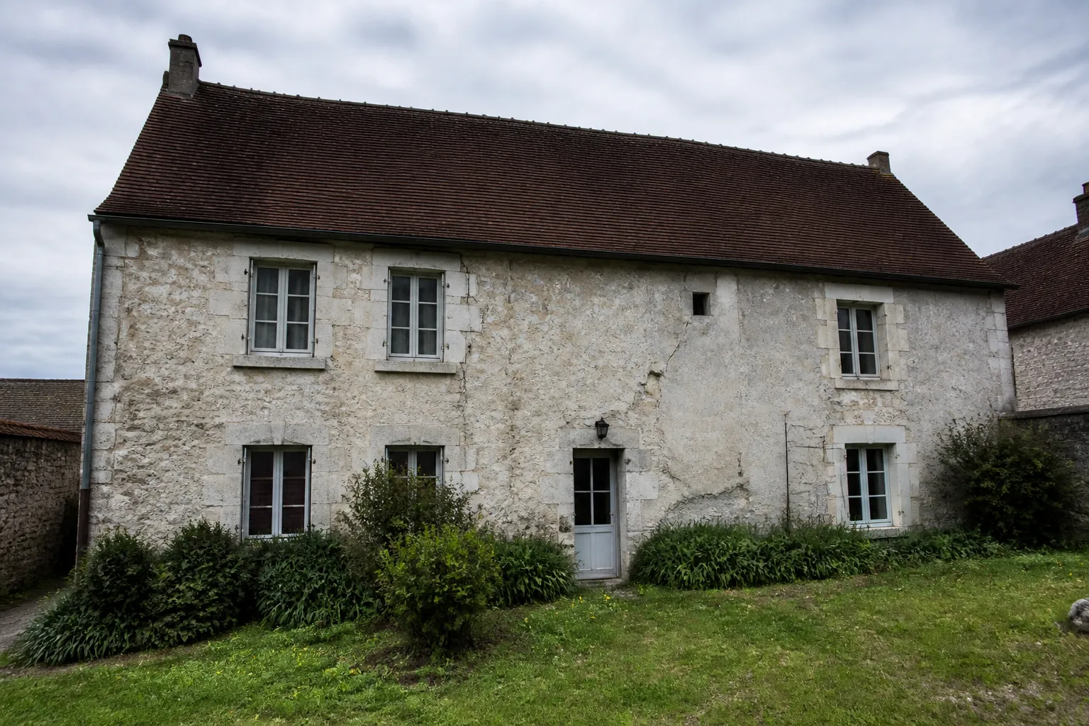 Maison ancienne en pierre avec fissures visibles sur la façade, vue depuis le jardin